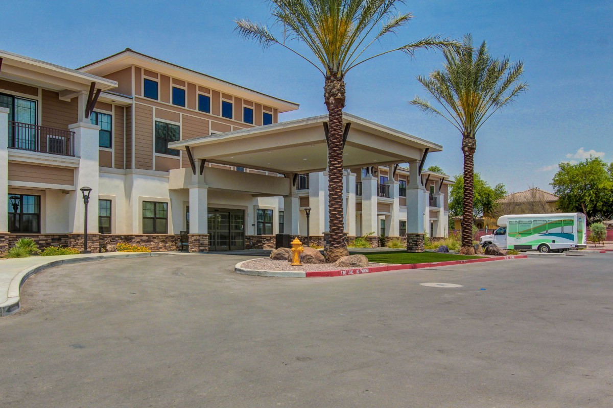 A modern building with a covered entrance and palm trees lining the driveway.