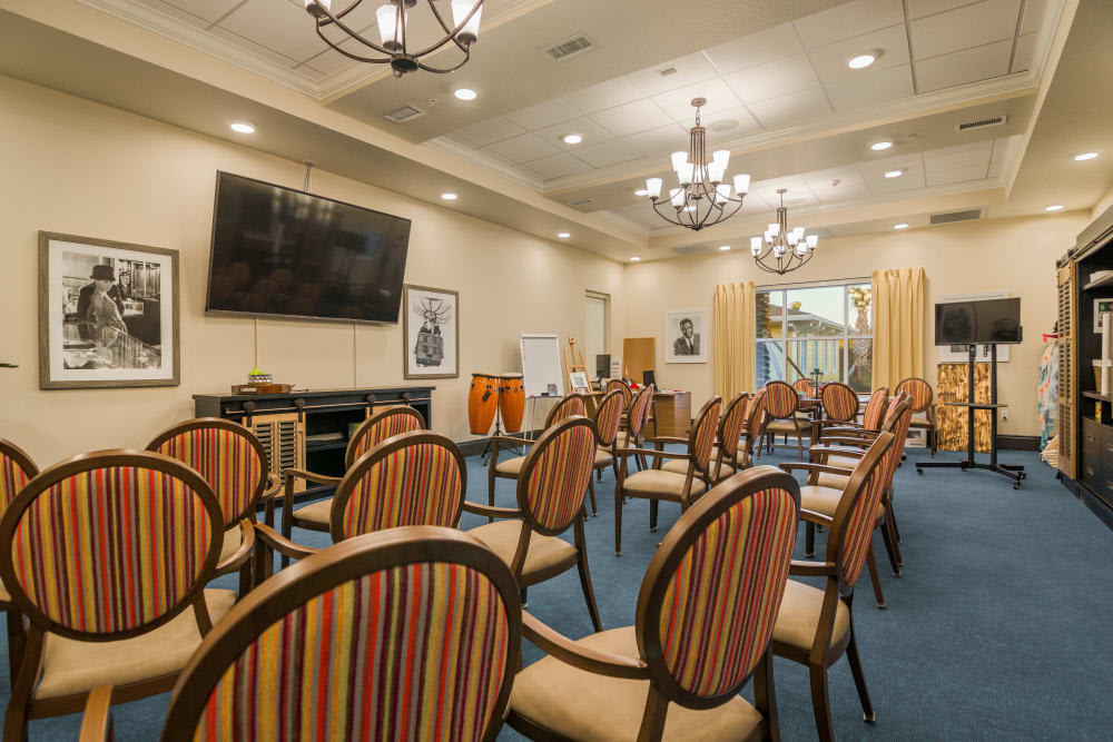 An empty conference room with striped chairs arranged in rows, a large television, and chandeliers overhead.