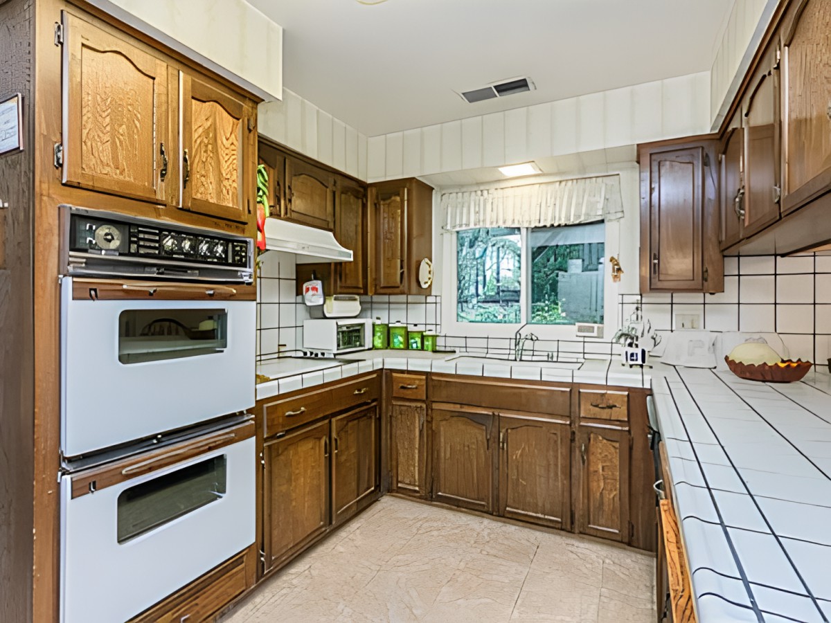 A retro-style kitchen with wooden cabinets, tile countertops, and a double oven.