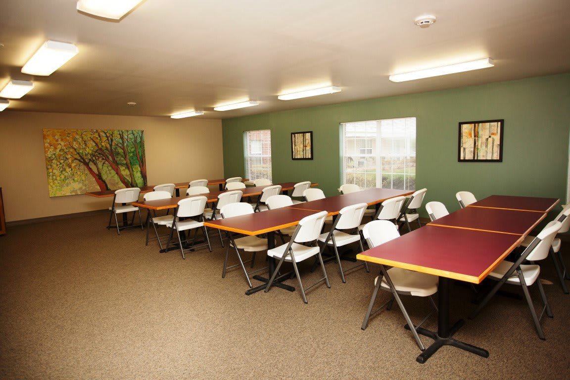 An empty classroom with tables and chairs arranged neatly, featuring artwork on the walls.