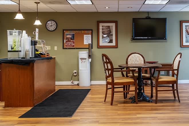 A cozy office break room with tables, chairs, a water cooler, and a TV on the wall.