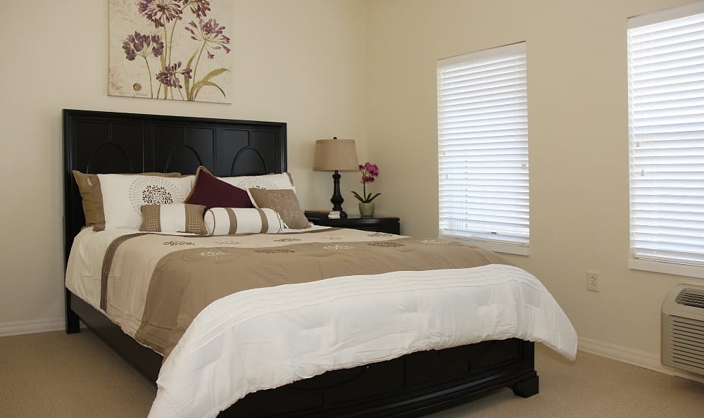 A cozy bedroom with a neatly made bed, bedside lamp, and window blinds.