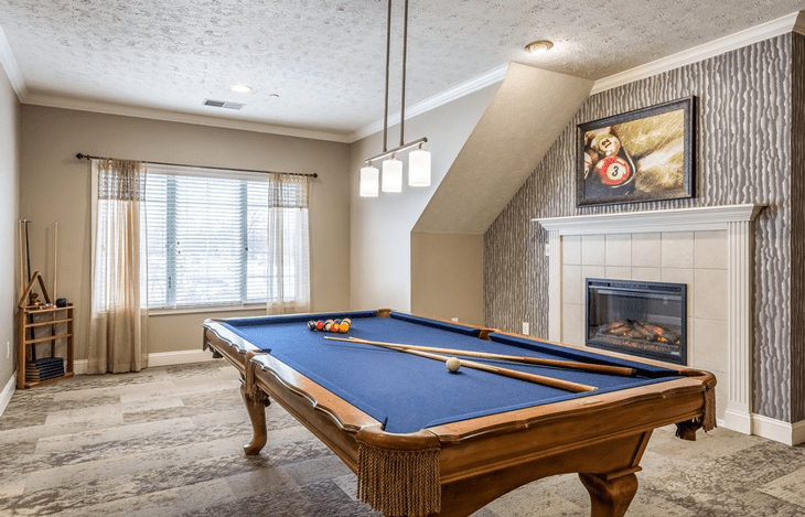 A stylish game room featuring a billiard table with blue felt, complemented by modern overhead lighting and a cozy fireplace.