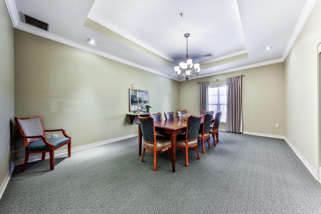 A spacious dining room with a long wooden table, surrounded by chairs and illuminated by a chandelier.