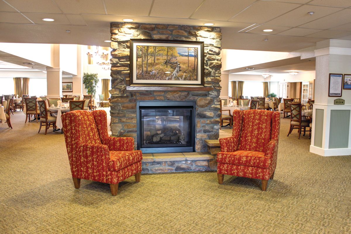 A cozy lounge area featuring a stone fireplace flanked by two red patterned chairs.