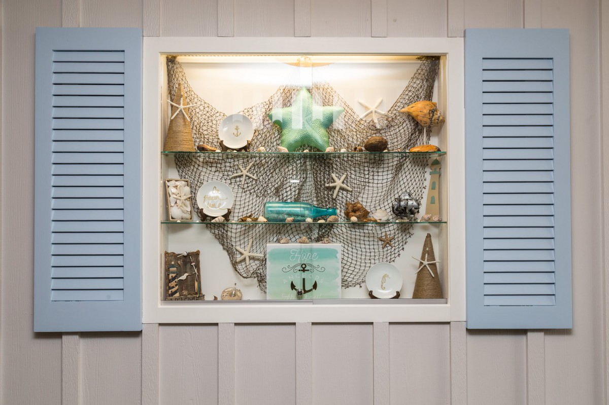 A nautical-themed display featuring seashells, starfish, and an anchor against a backdrop of fishing net with blue shutters.