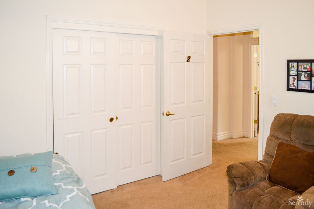 A bedroom interior featuring white closet doors, a partially open door, carpeted floor, and a glimpse of furniture.