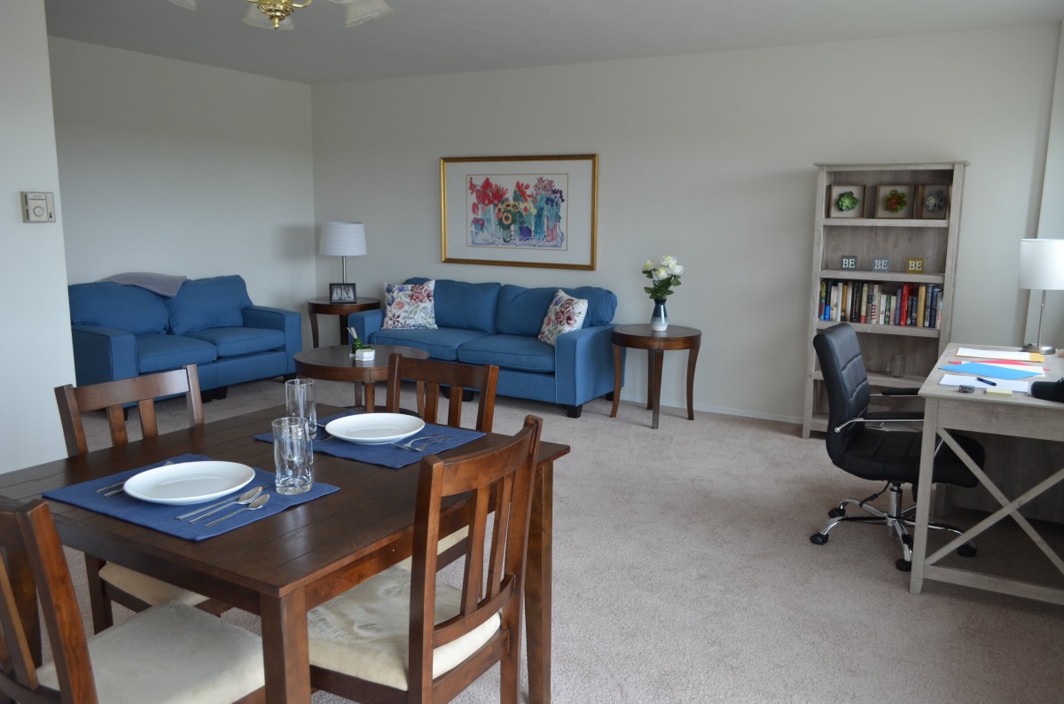 A cozy living and dining area featuring blue sofas, a dining table, and a bookshelf.