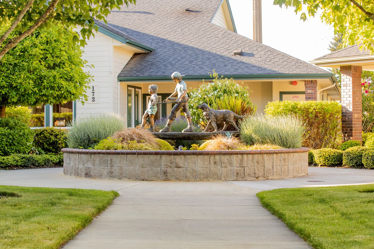 A garden with a sculpture of children and a dog in front of a house.