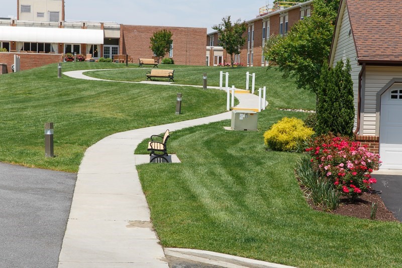 A winding pathway with benches, surrounded by well-maintained grass and landscaping, leading towards buildings.