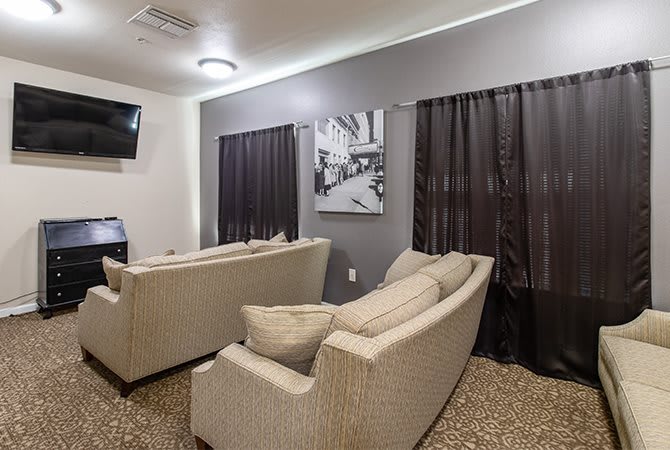 A cozy living room with beige couches facing a television and artwork on the wall.