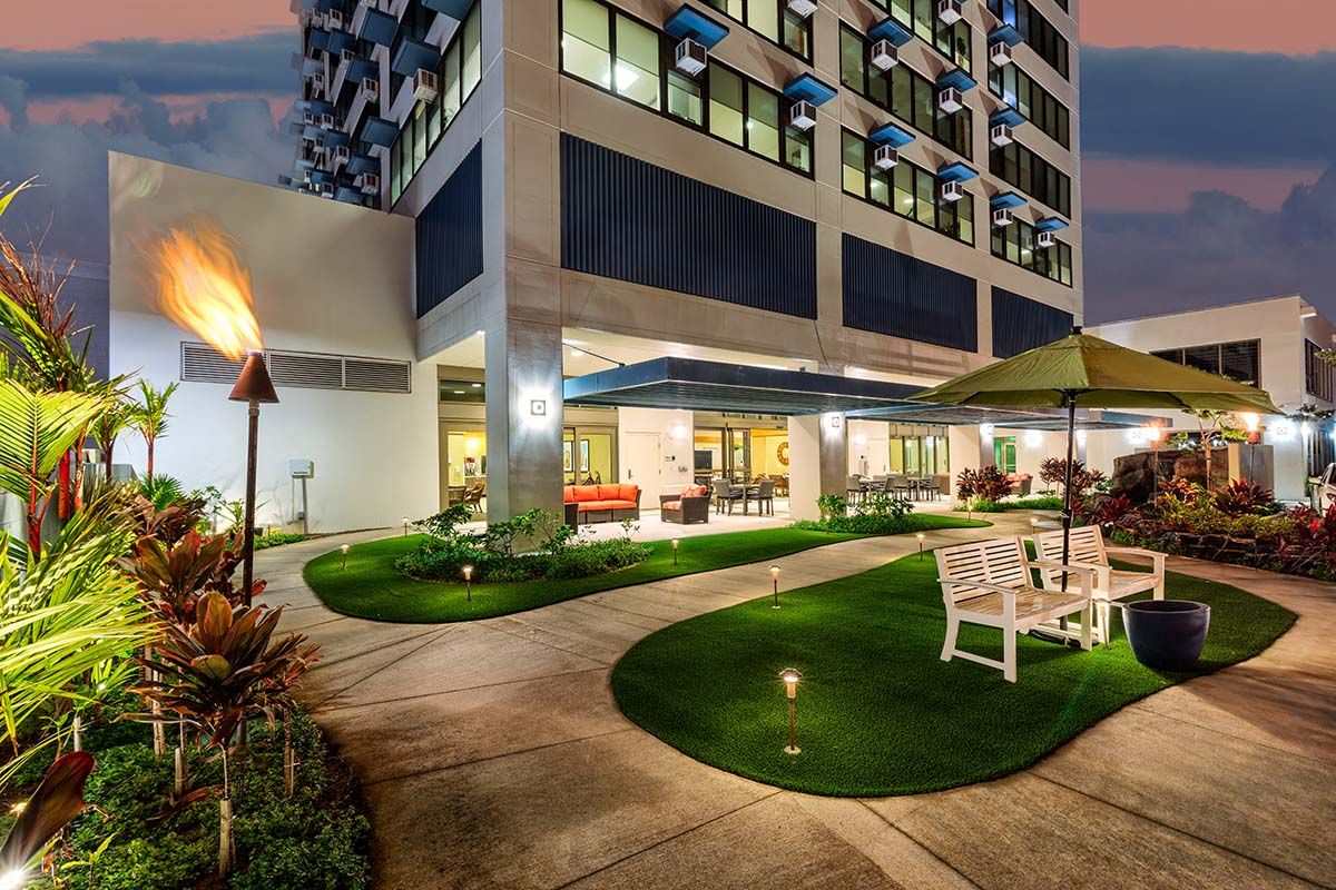 A beautifully lit hotel exterior with a landscaped garden and outdoor seating area at night.