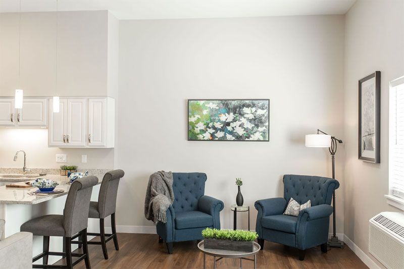 A cozy living room with two blue chairs, a table, and artwork on the wall.
