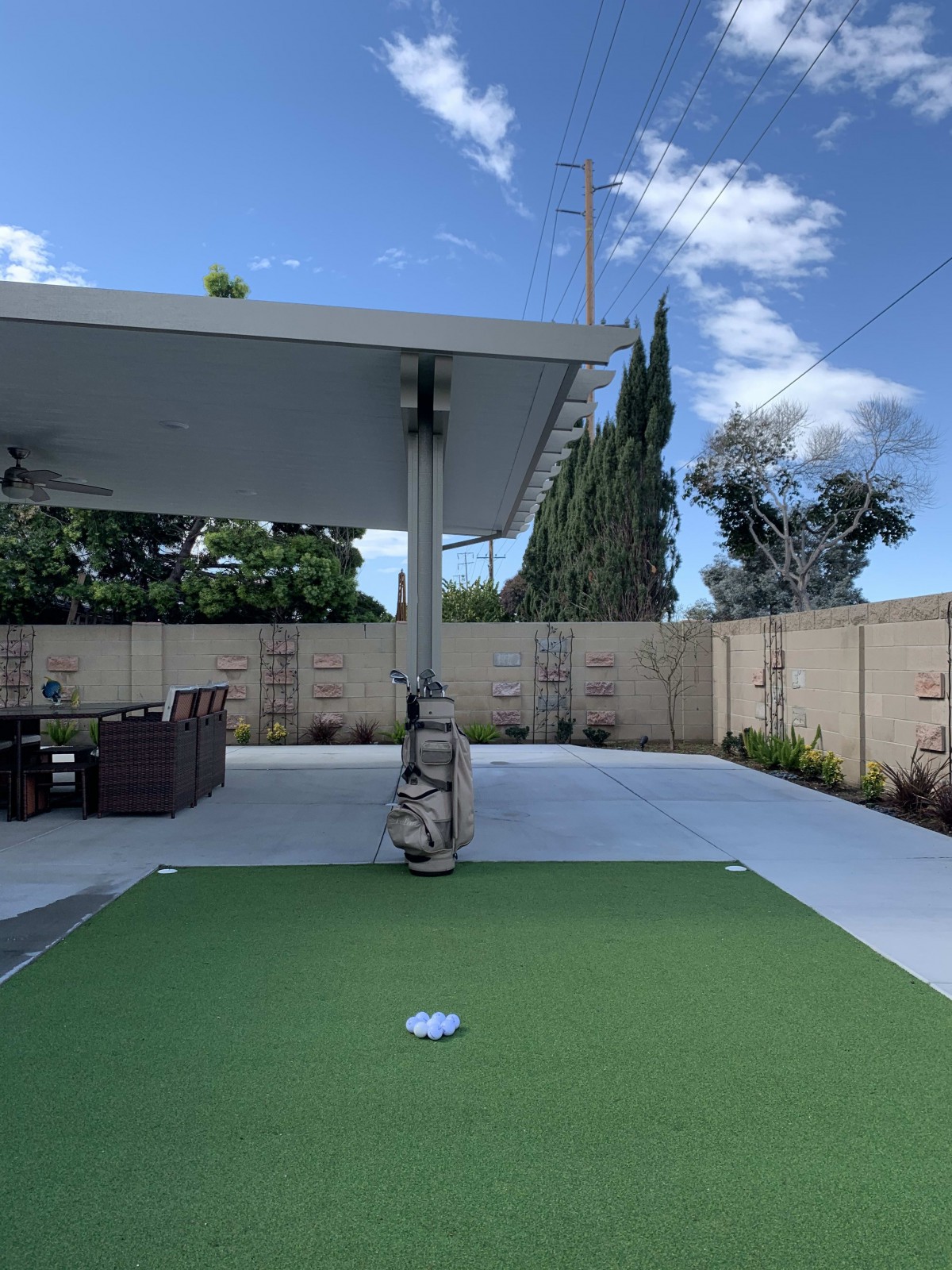 A backyard patio featuring a putting green and outdoor furniture under a covered area.