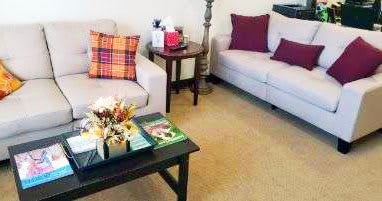 A cozy living room with sofas and a coffee table adorned with magazines and floral decor.