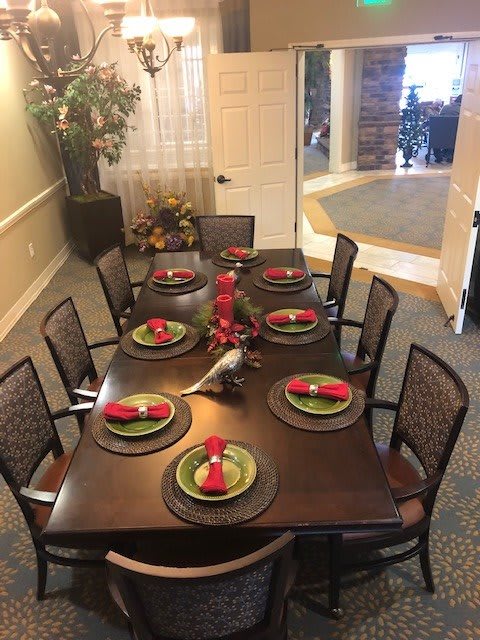 A neatly set dining table with plates and red napkins, surrounded by chairs.