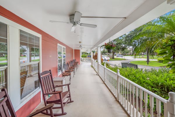 A spacious covered porch with rocking chairs and a ceiling fan, offering a relaxing outdoor seating area beside a red exterior wall.