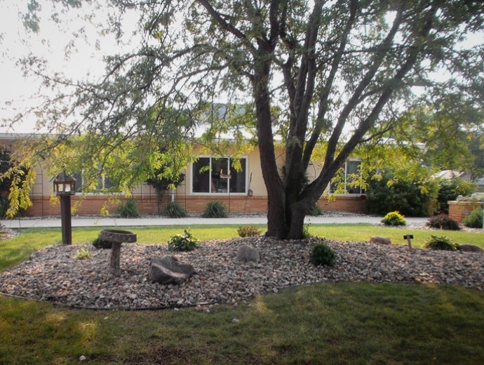 A view of a house with a landscaped front yard featuring a large tree and decorative rocks.