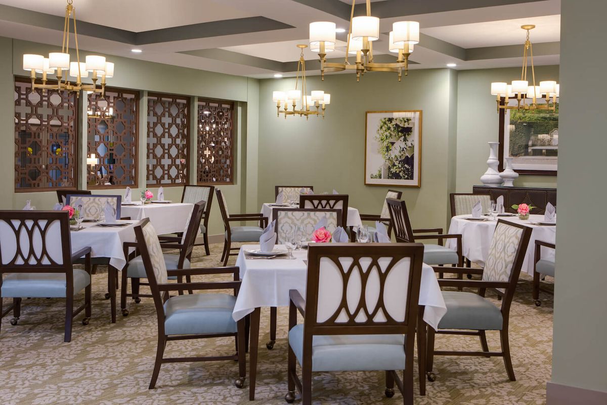 An elegant dining room with neatly arranged tables and chairs, illuminated by chandeliers.