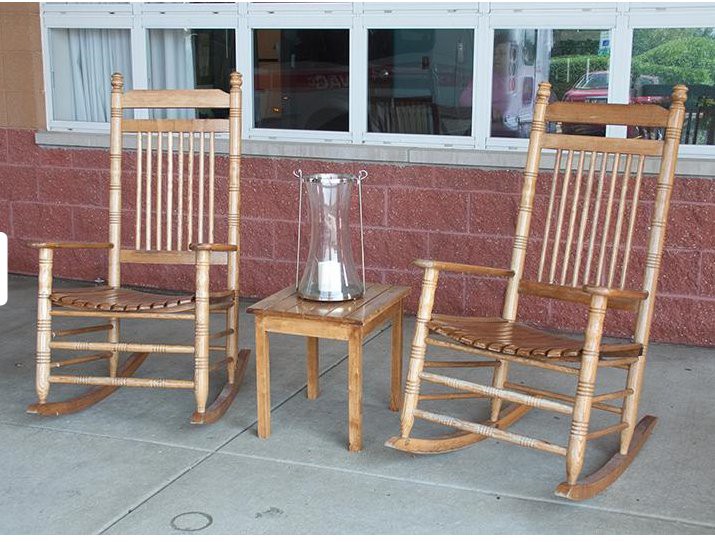 Two wooden rocking chairs with a small table holding a candlestick between them on an outdoor porch.