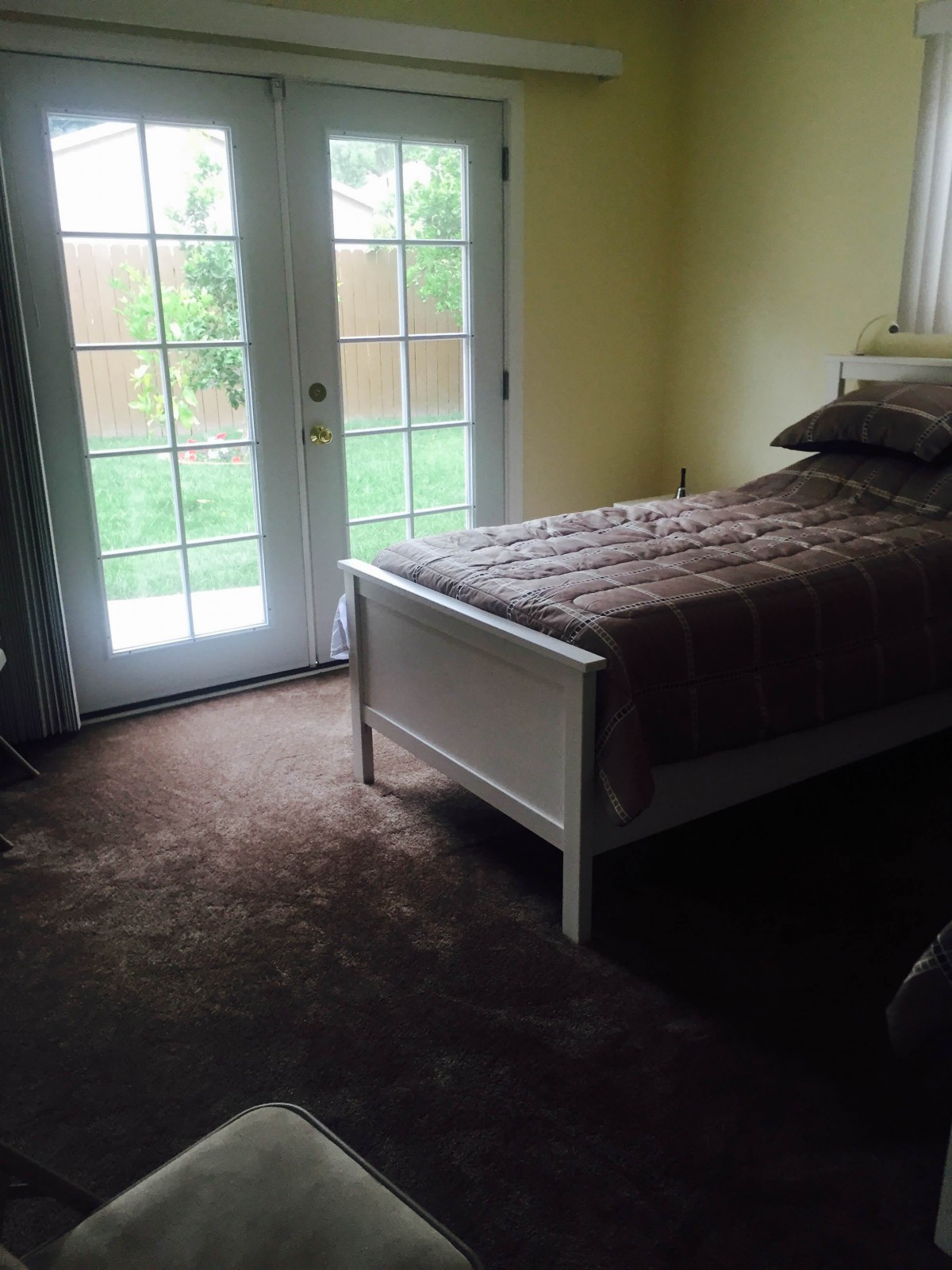A cozy bedroom with a single bed and French doors opening to a garden.