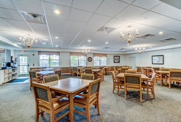 A spacious dining area with multiple tables and chairs, illuminated by chandeliers and natural light from large windows.