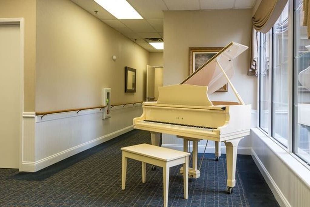 A white grand piano is placed in a well-lit hallway with framed pictures on the walls.