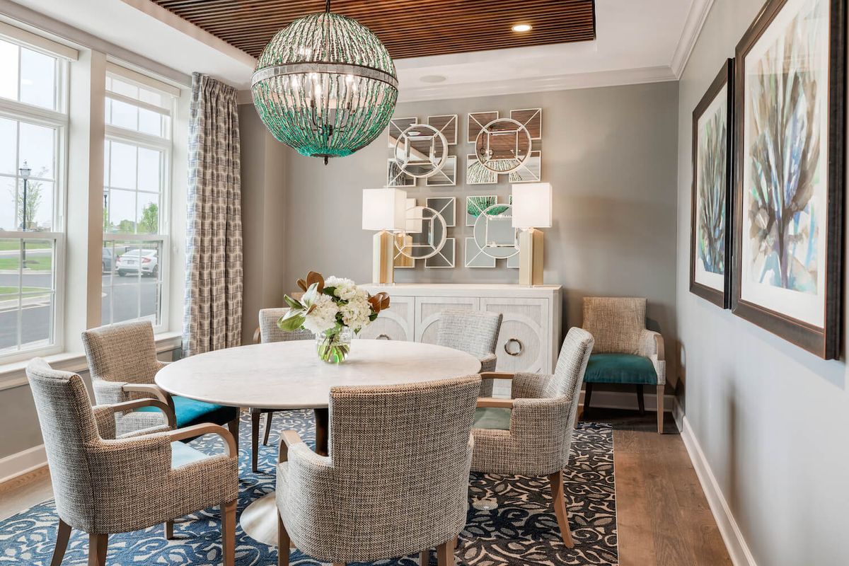 A modern dining room with a round table, upholstered chairs, and an elegant chandelier.
