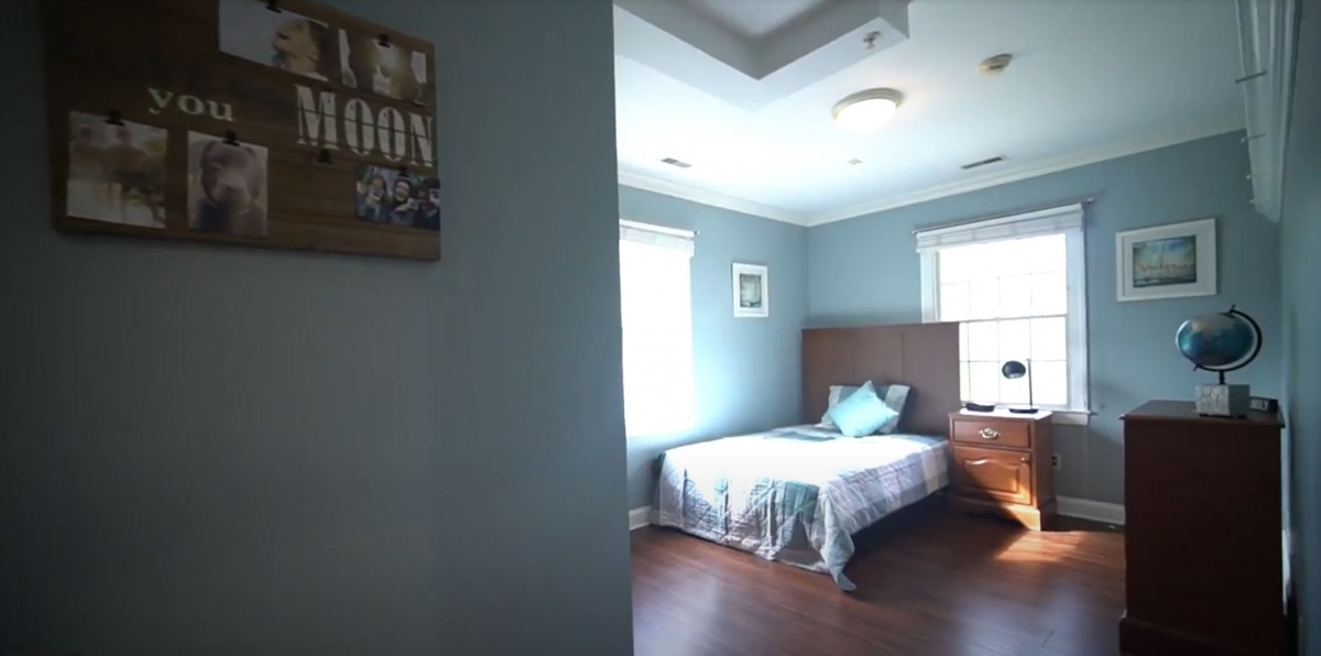 A cozy bedroom with blue walls, featuring a bed with pillows and a bedside table.
