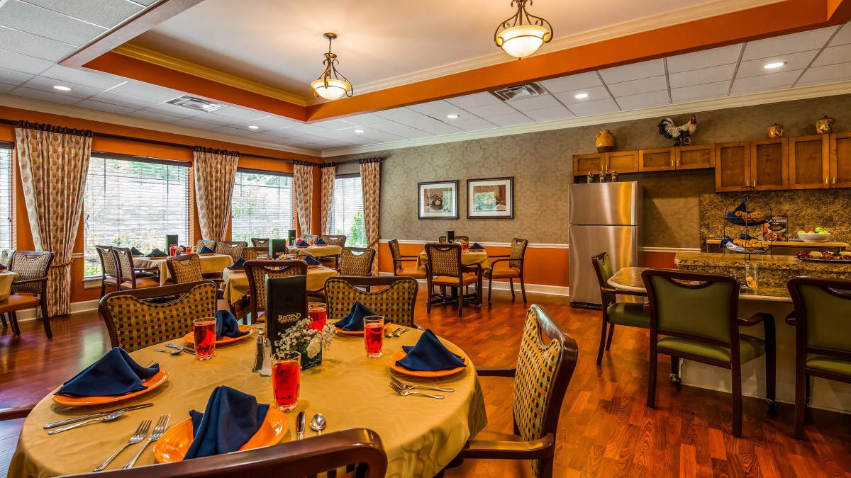 A warmly decorated dining room with neatly arranged tables and chairs, featuring elegant lighting and wooden flooring.