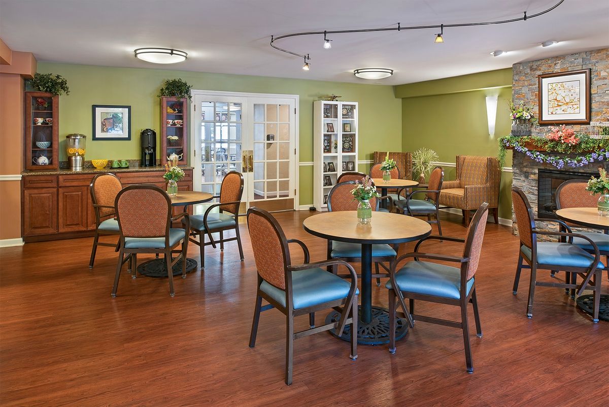 A cozy seating area with tables and chairs, featuring green walls and wood flooring.