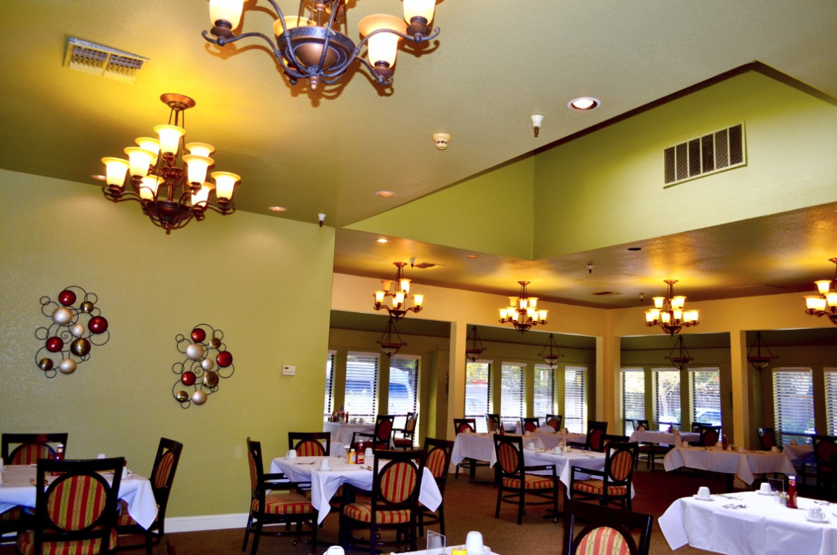 A spacious dining room with elegant chandeliers and neatly arranged tables and chairs.