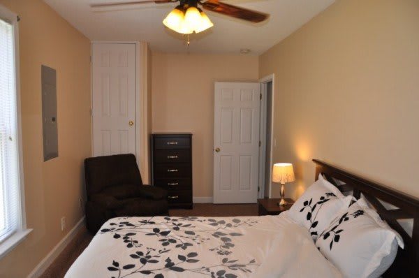A cozy bedroom featuring a bed with floral bedding, a lamp on the nightstand, and a dresser against the wall.