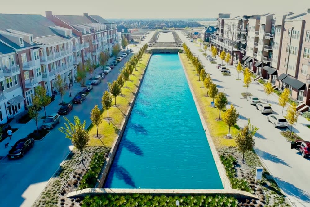 An urban canal flanked by buildings and trees on a sunny day.