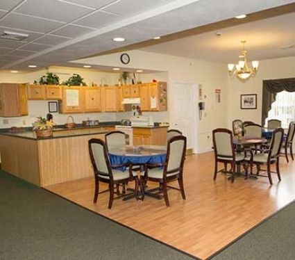 A spacious kitchen and dining area with wooden floors, tables, and chairs under a chandelier.