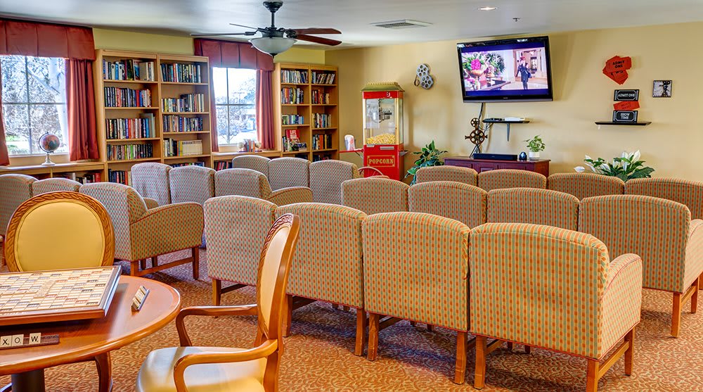 A cozy room with rows of chairs facing a television, surrounded by bookshelves and featuring a popcorn machine.