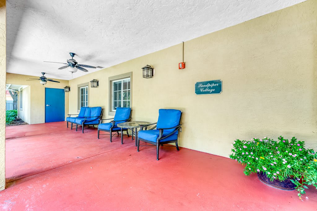 A cozy patio area with blue chairs and tables against a yellow wall.