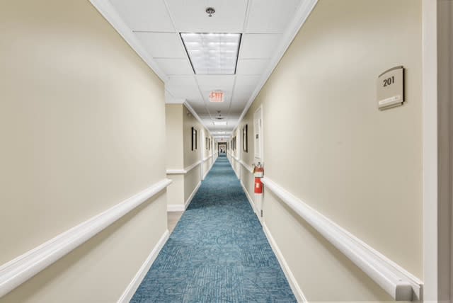 A long, empty hallway with beige walls and blue carpet.