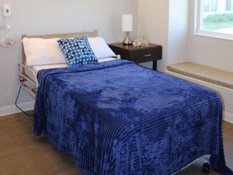 A neatly made bed with a blue blanket and a decorative pillow in a cozy bedroom setting.