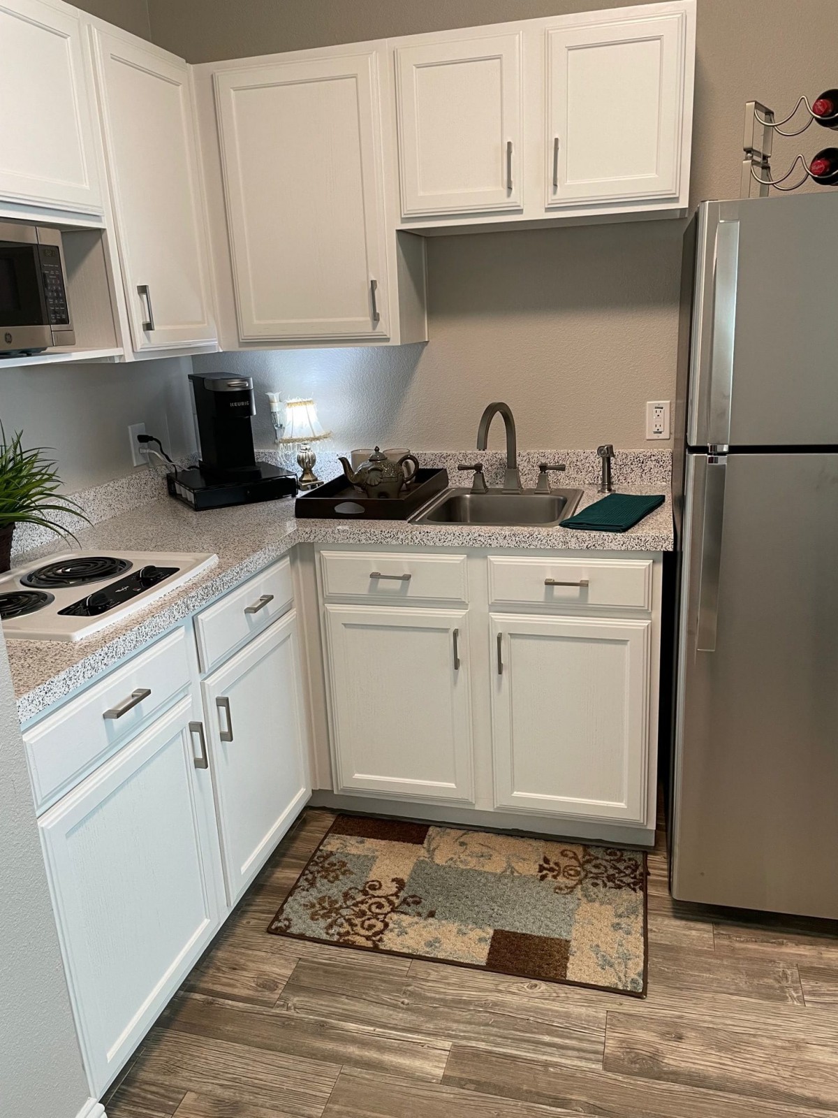 A compact kitchen with white cabinets, a stainless steel refrigerator, and various appliances.