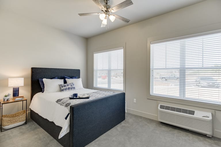 A minimalist bedroom with a bed, two windows, and a ceiling fan.