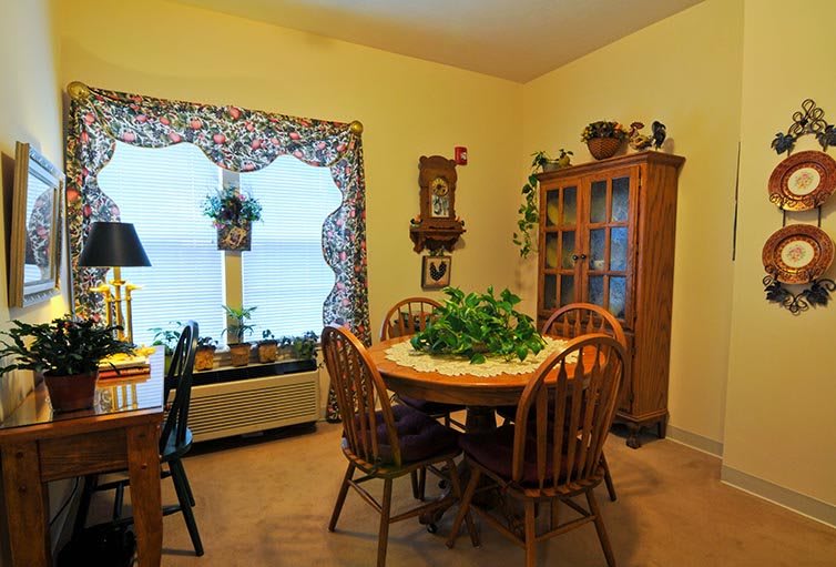 A cozy dining area featuring a round wooden table with chairs, surrounded by a cabinet and window adorned with decorative elements and plants.