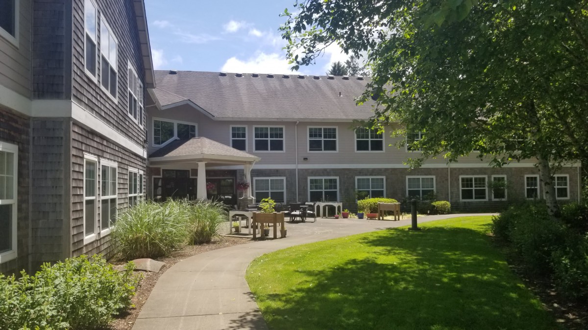 A sunny view of a two-story building with a garden and pathway.
