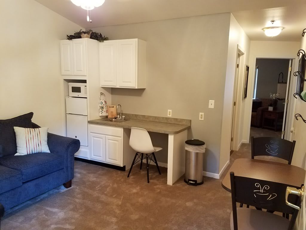 A cozy living area with a kitchenette, featuring a blue sofa and white cabinets.