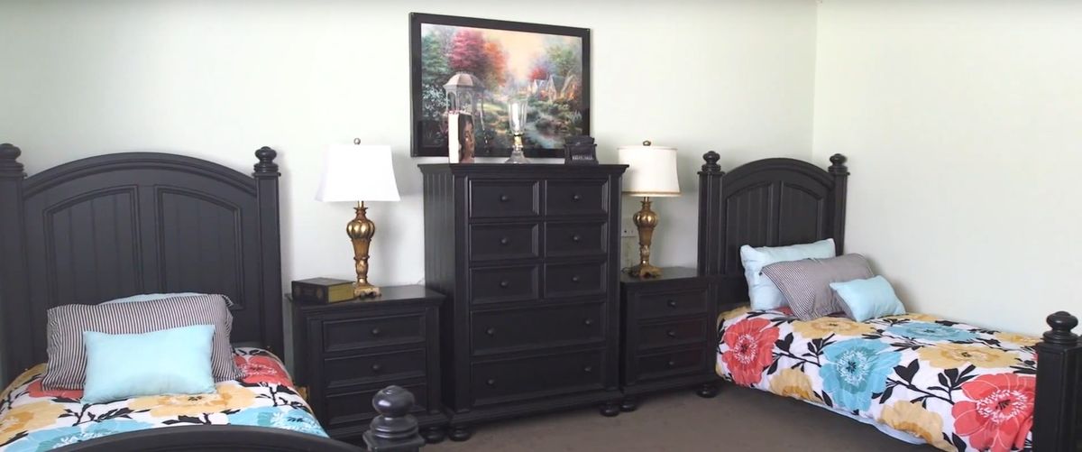 A well-furnished bedroom with a black dresser, matching nightstands, decorative lamps, and a colorful painting above.