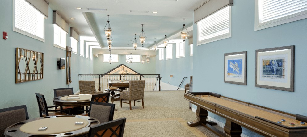 A spacious and modern lounge area with a shuffleboard table, ample seating, and natural lighting.