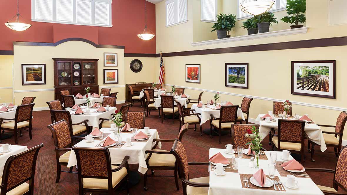 A well-decorated dining room with neatly arranged tables and chairs, featuring artwork on the walls and plants for ambiance.