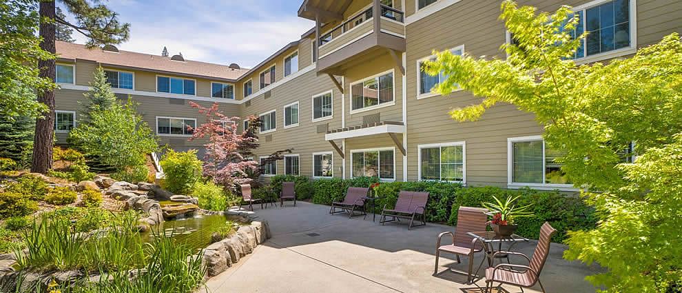 A view of a residential building with an outdoor patio area featuring chairs and lush landscaping.