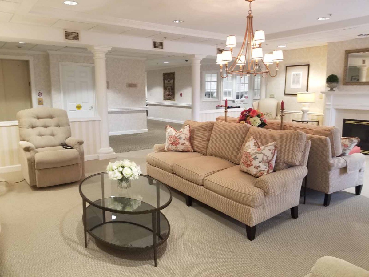A cozy and elegantly decorated living room with a sofa, glass coffee table, and chandelier.