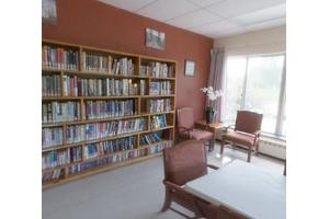 A cozy reading area with bookshelves, chairs, and a table near a large window.
